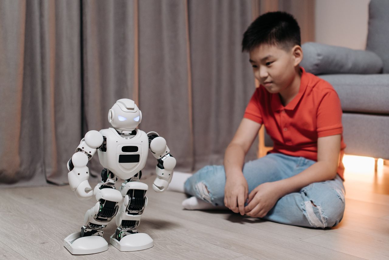 The Art of Drawing Readers In: Your attractive post title goes here An asian boy sitting on the floor, interacting with a white robot, showcasing innovation and technology.